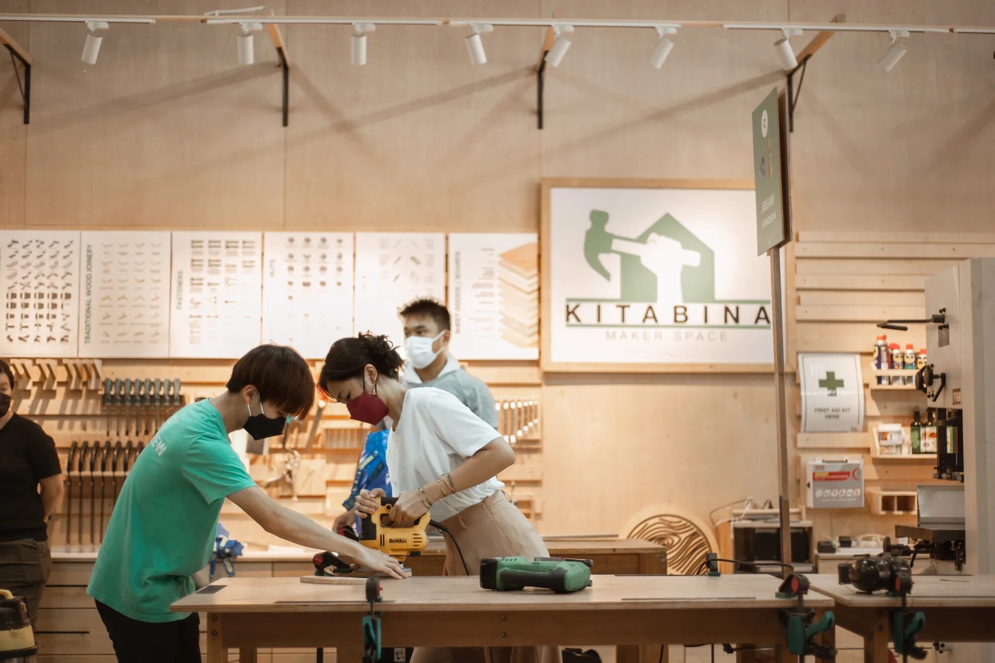 A KitaBina facilitator guiding a maker through a jigsaw cut at the table, with others working alongside